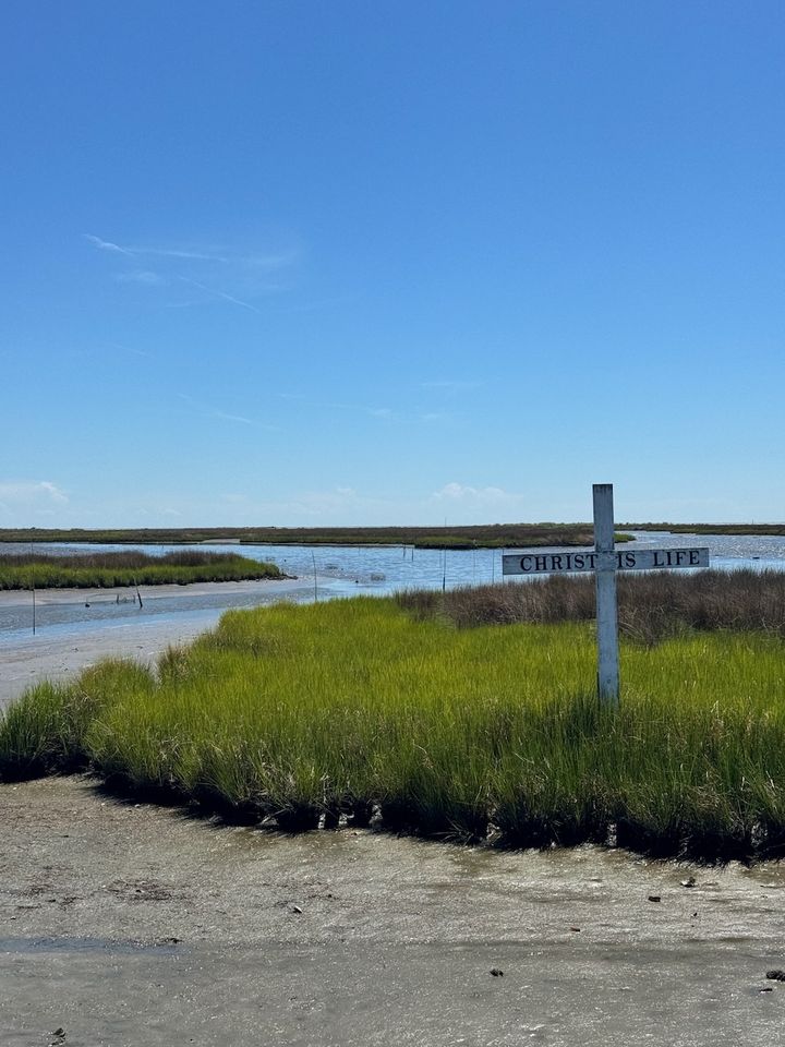A narrow waterway through the marshes of Tangier Island under a clear blue sky.