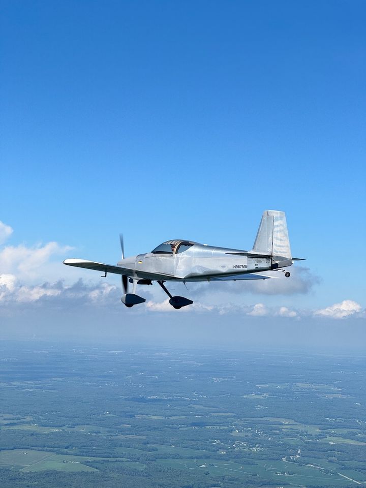 A silver RV-7 flying in formation against a blue sky.