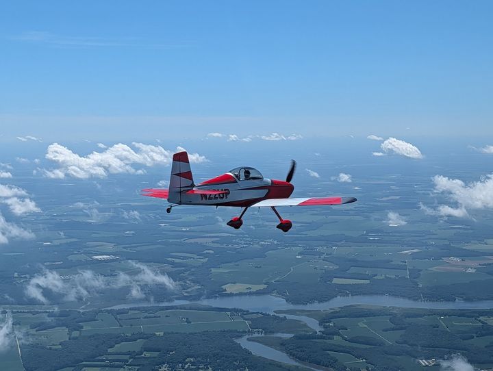 A red RV flying in formation above patchwork farmland.