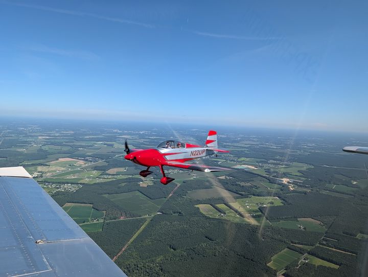 A red RV flying in close formation over patchwork farmland.